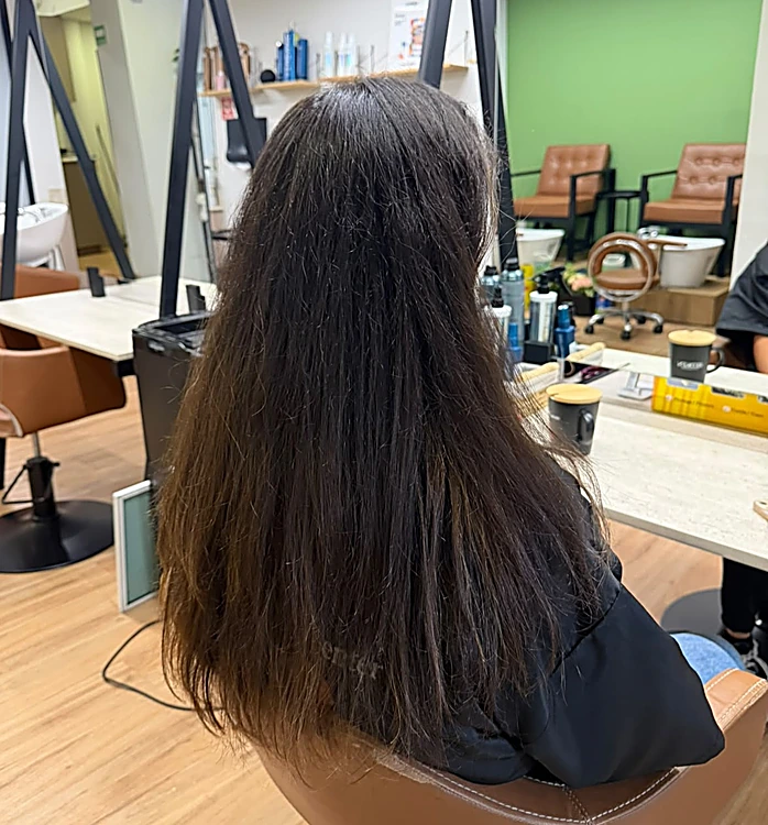 Antes: cabello largo castaño oscuro sin color, de espaldas en el salón